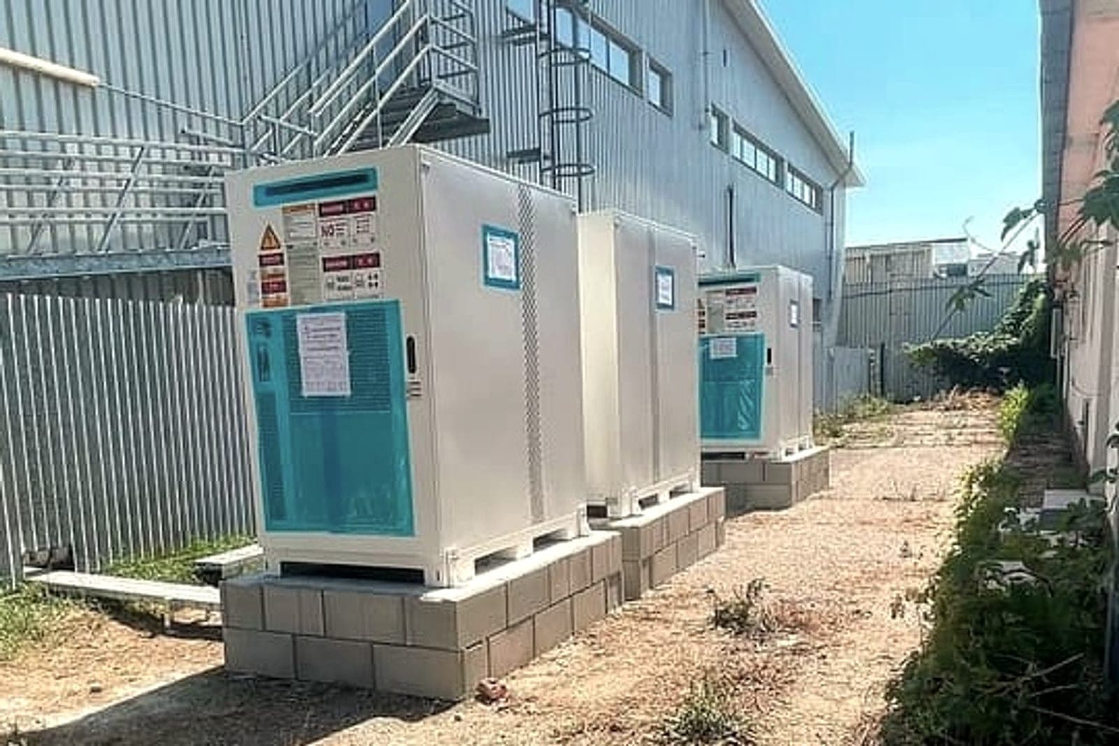 Three battery storage cabinets on concrete plinths next to a hall