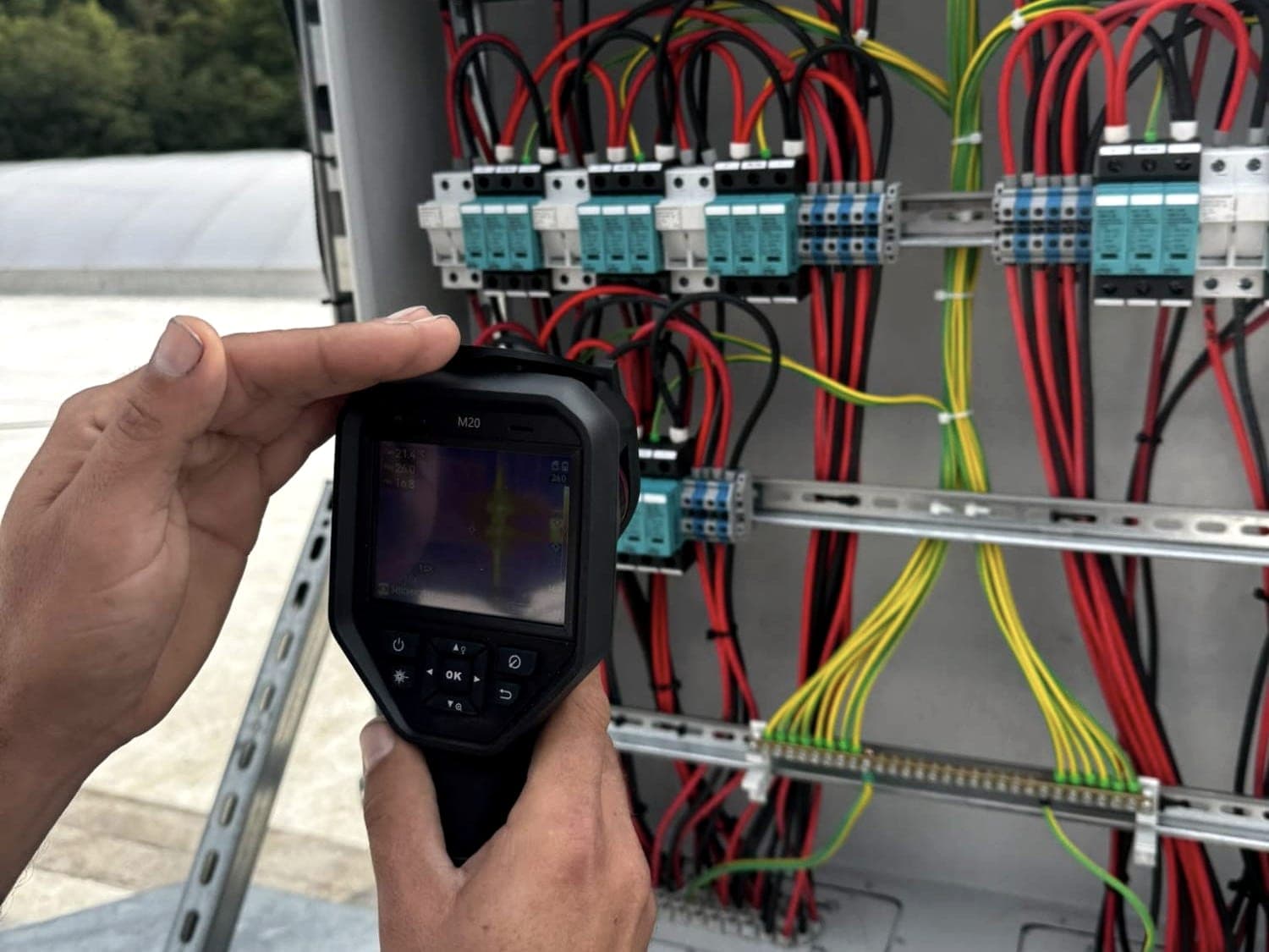 Technician checking a PV DC combiner box with surge protection using a thermal camera