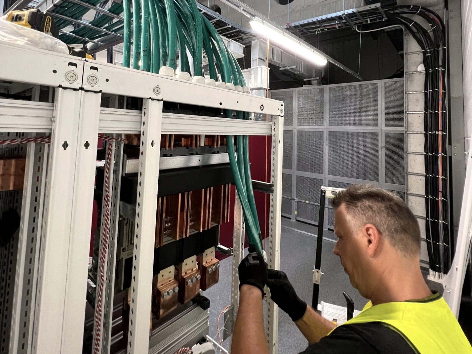 Electrician connecting power cables to a main LV switchboard with copper busbars